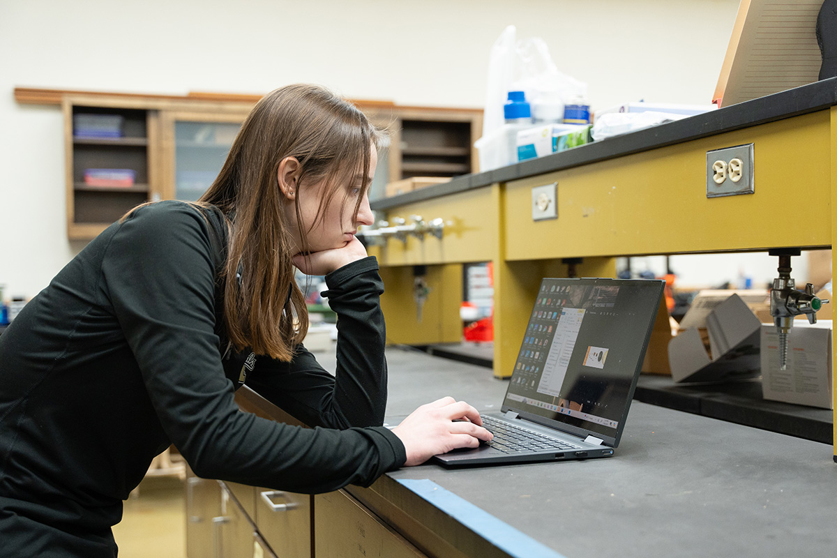 Woman in a lab leans over a laptop.
