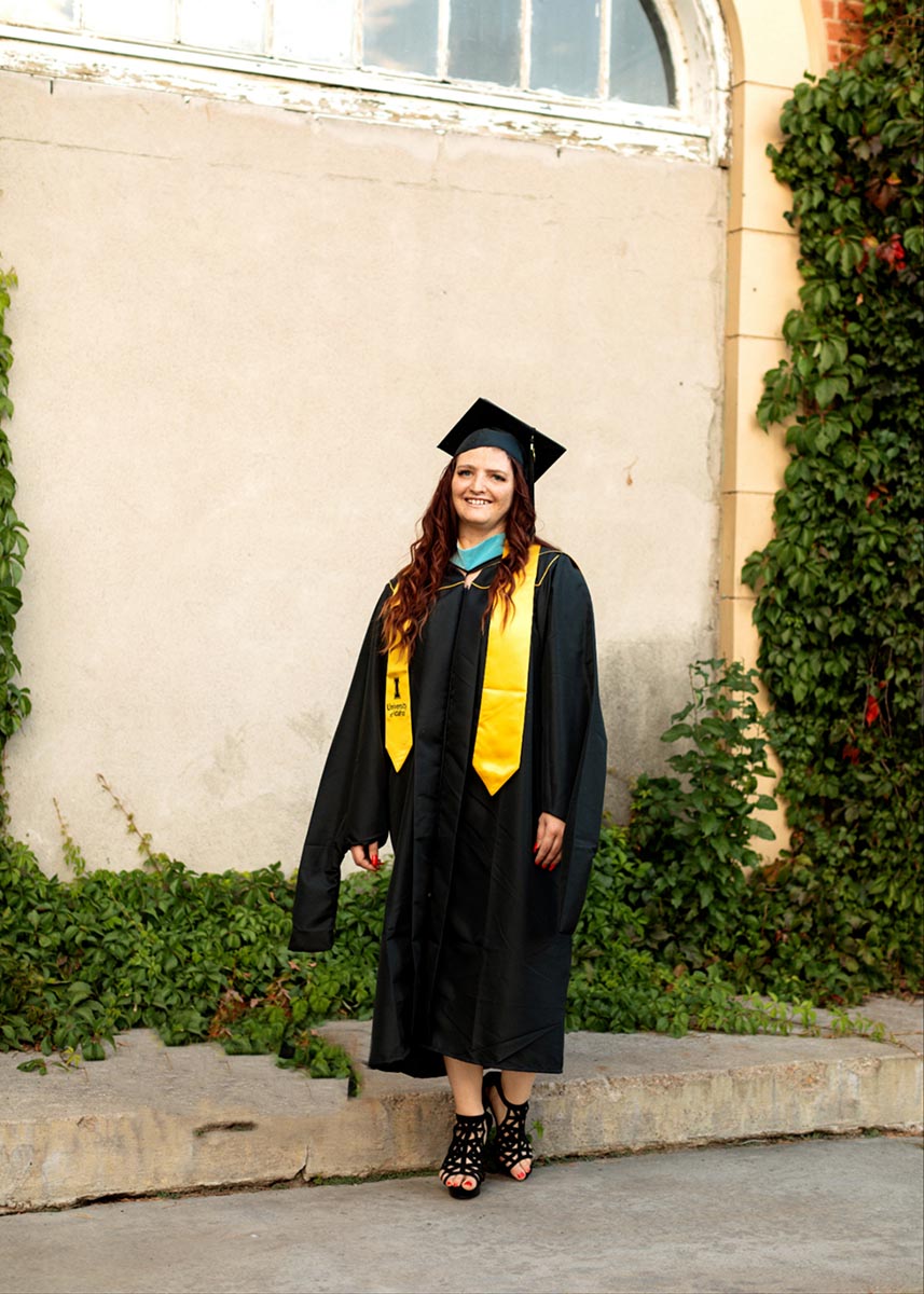 Woman in cap and gown standing in front of building.