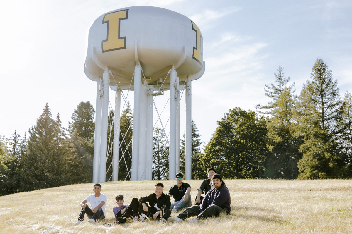 A group of Sigma Lambda Beta students sit in grass beneath a water tower with the university's block I logo.