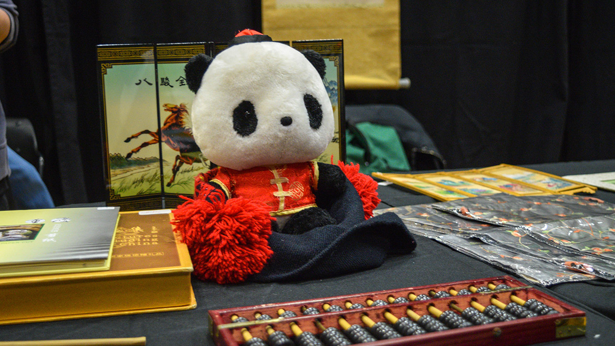Several books on China, as well as a stuffed panda bear dressed in traditional clothing, an abacus, as well as panel artwork depicting a horse in a field.  
