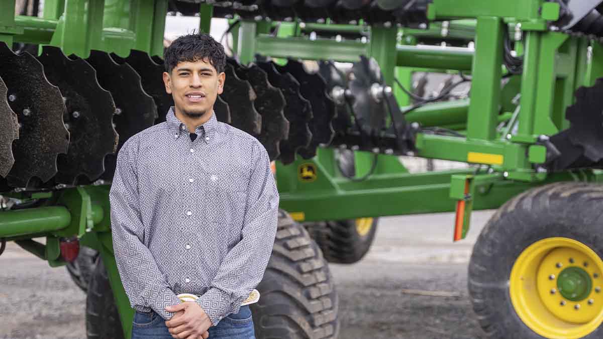 A man stands in front of a large John Deere combine.