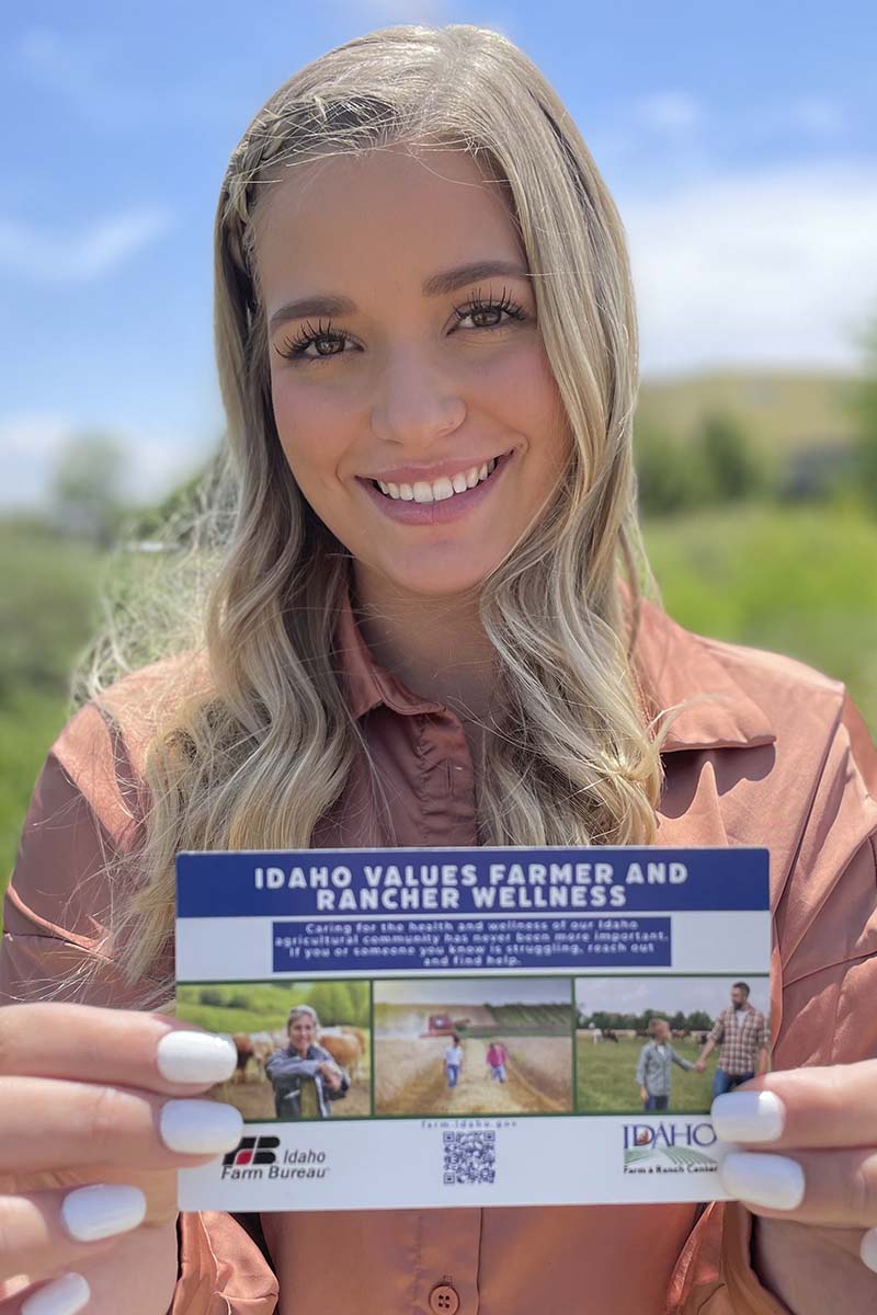 A woman holds a postcard advertising a farmer and rancher wellness program.