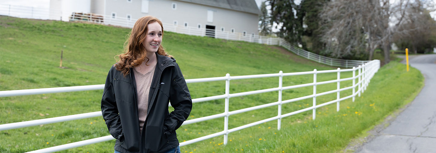 A person standing next to a white fence with a white barn in the background.
