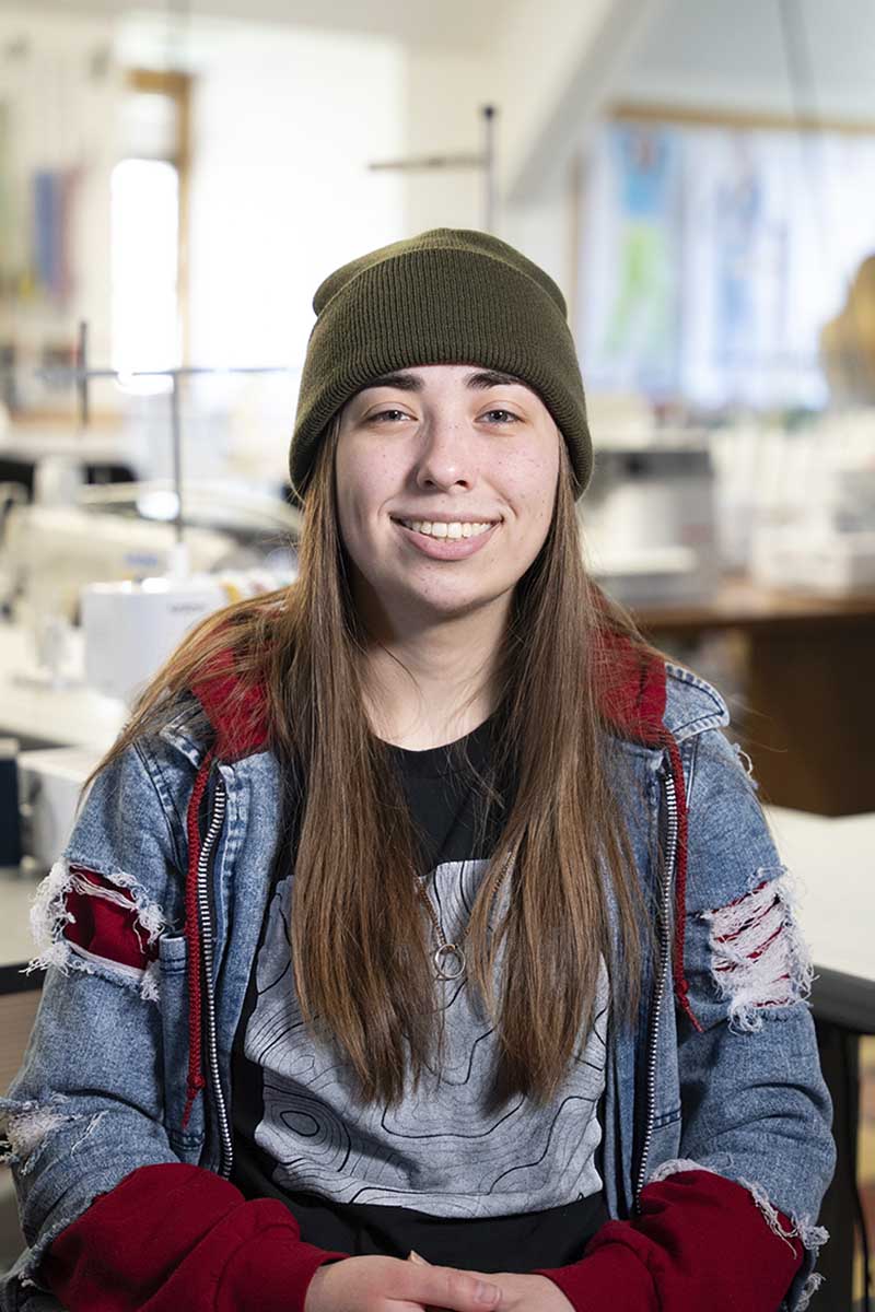 A headshot of a person wearing a beanie and a denim jacket.