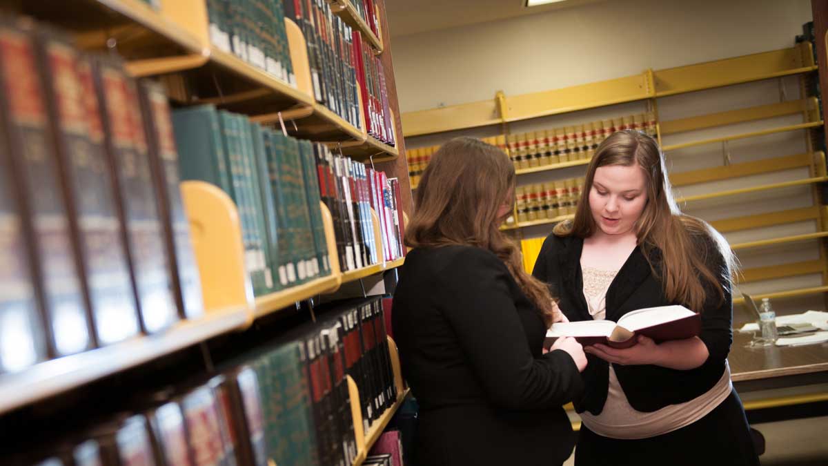 Two law students looking at a book near bookshelves in the library