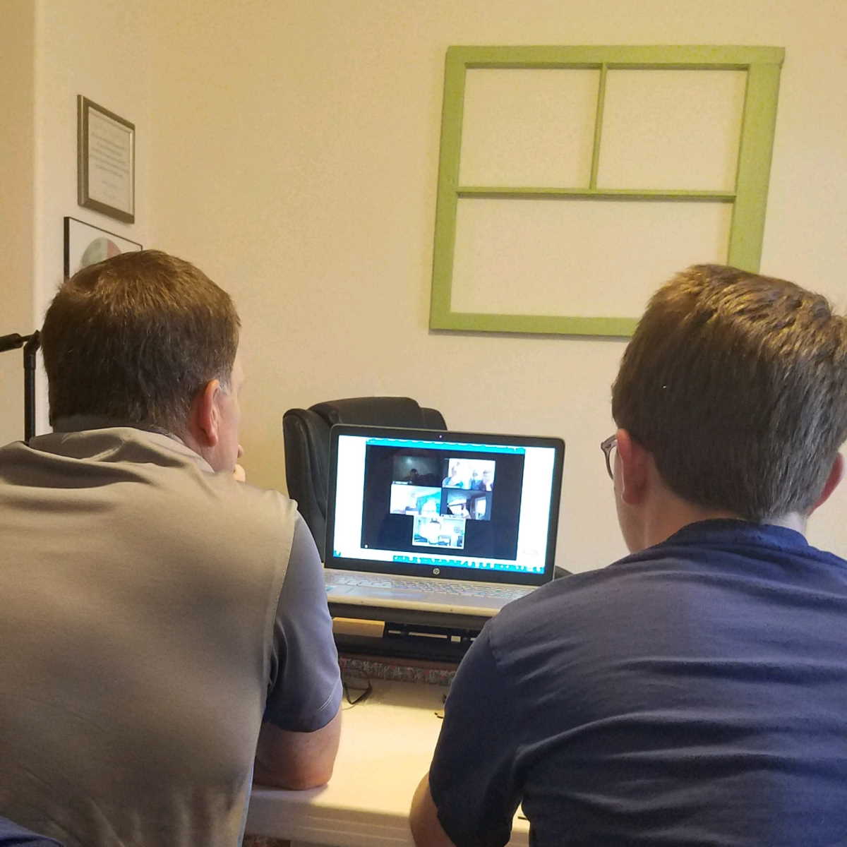 Two boys lean towards a computer screen.