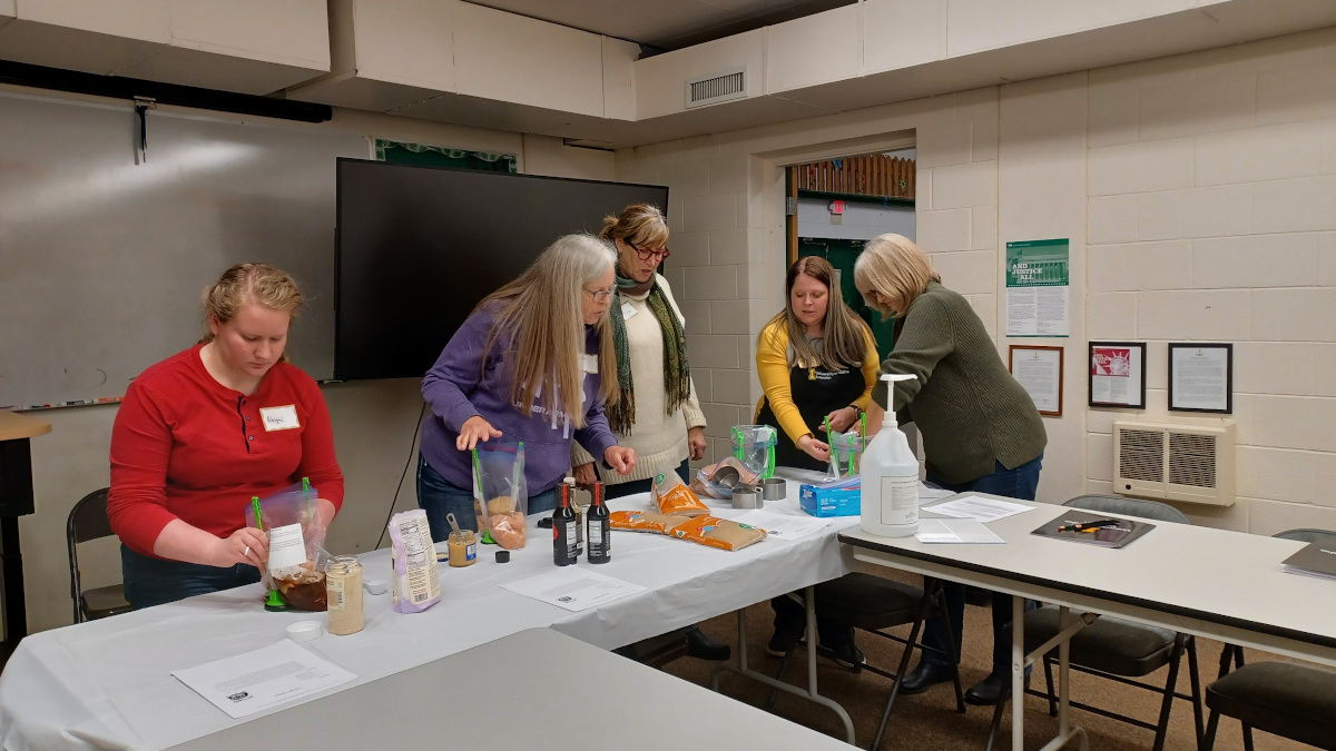 Adults prepare meals in a classroom environment.