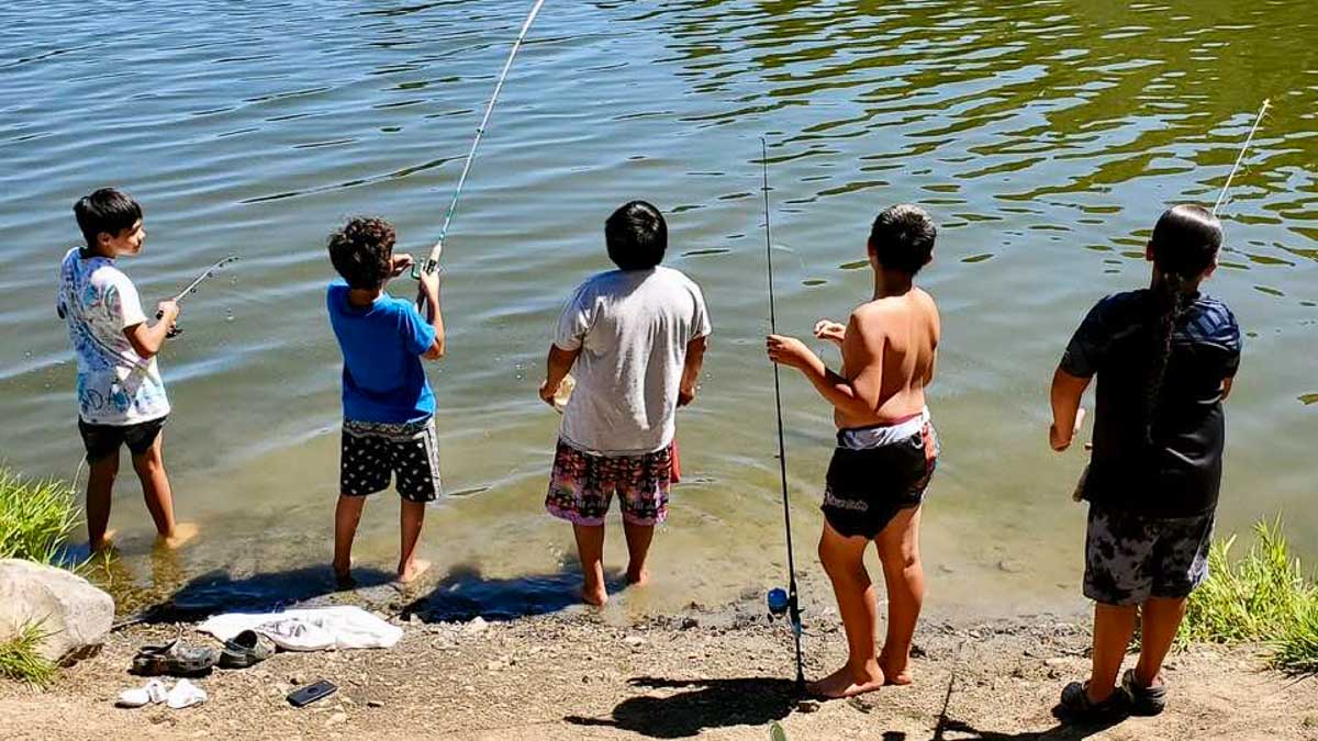 A group of youths fish at waters edge.