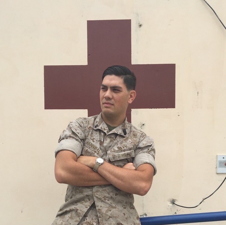 Man in military fatigues standing in front of a red cross.
