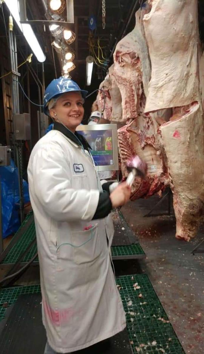 Woman in white lab coat standing next to a side of beef.