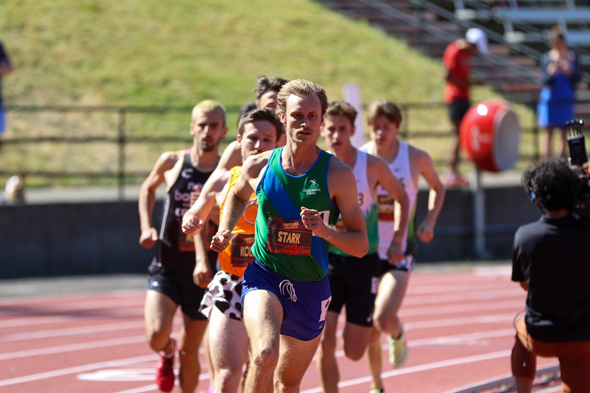 Man in blue and green jersey in front of group of runners