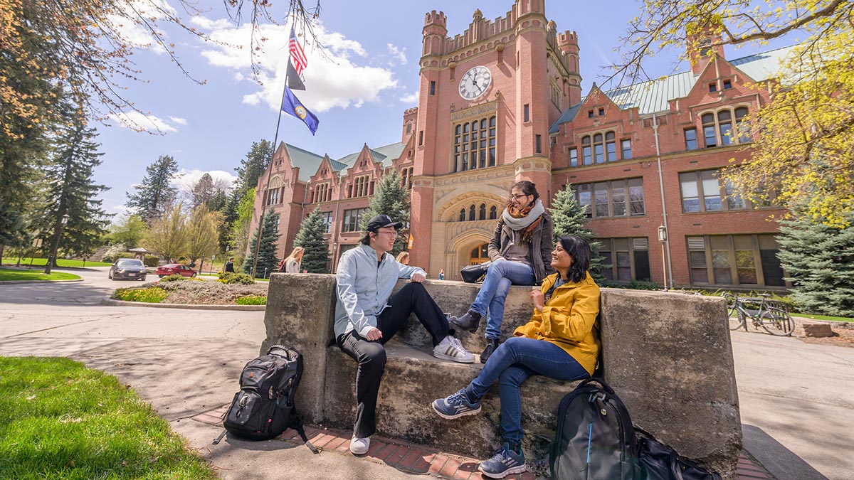 Three international students sit on the I-Bench outside the Admin Building.