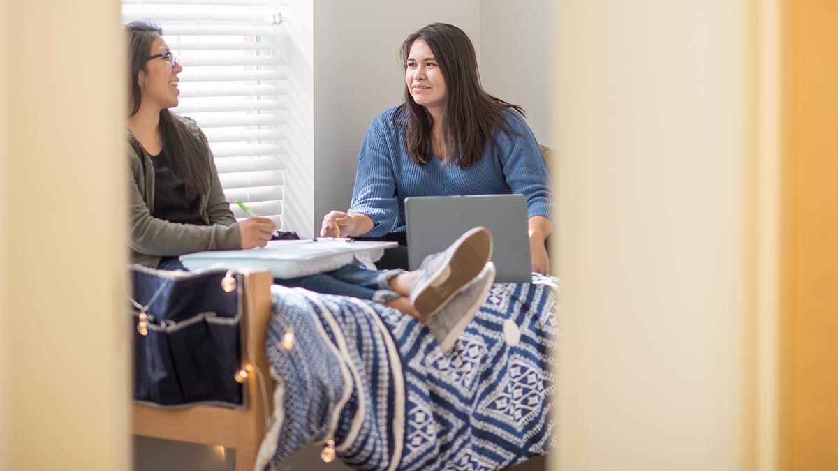 Two students studying in a dorm room as seen through the doorway