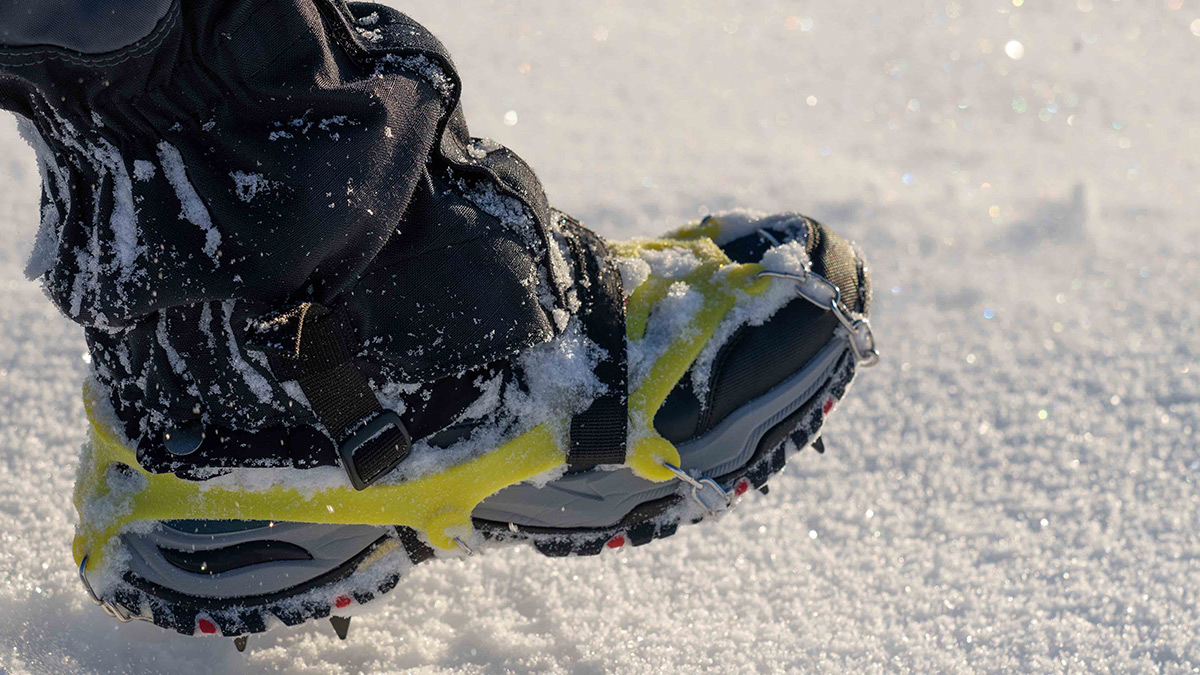 A shoe with traction device affixed, poised to step into snow.