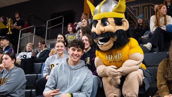 A male student smiling with Joe Vandal during a basketball game in the ICCU Arena.