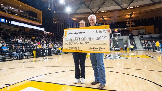 A student smiles as President Green awards them with a $1,000 scholarship during a basketball game in the ICCU arena. 