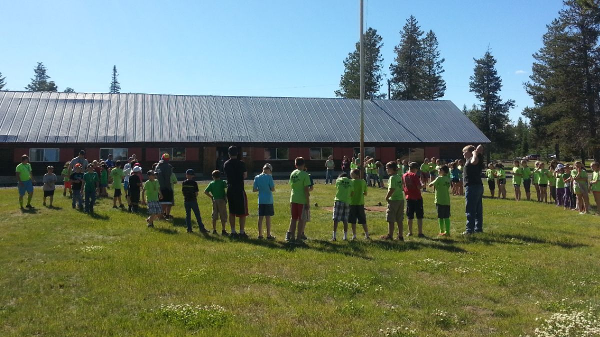 Dozens of children and teens standing in an arc on a grassy lawn.