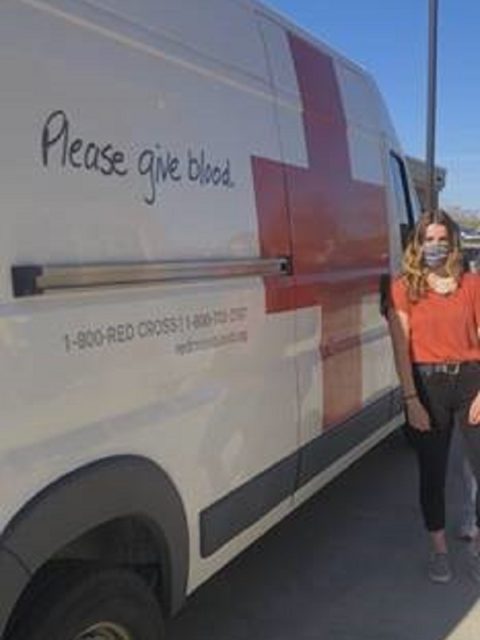 A girl standing next to a Red Cross van.