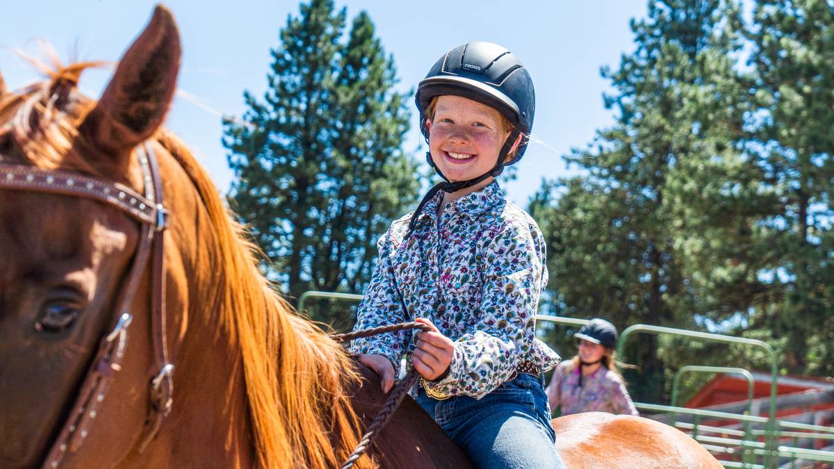 A child in a horse helmet grins from astride a horse.