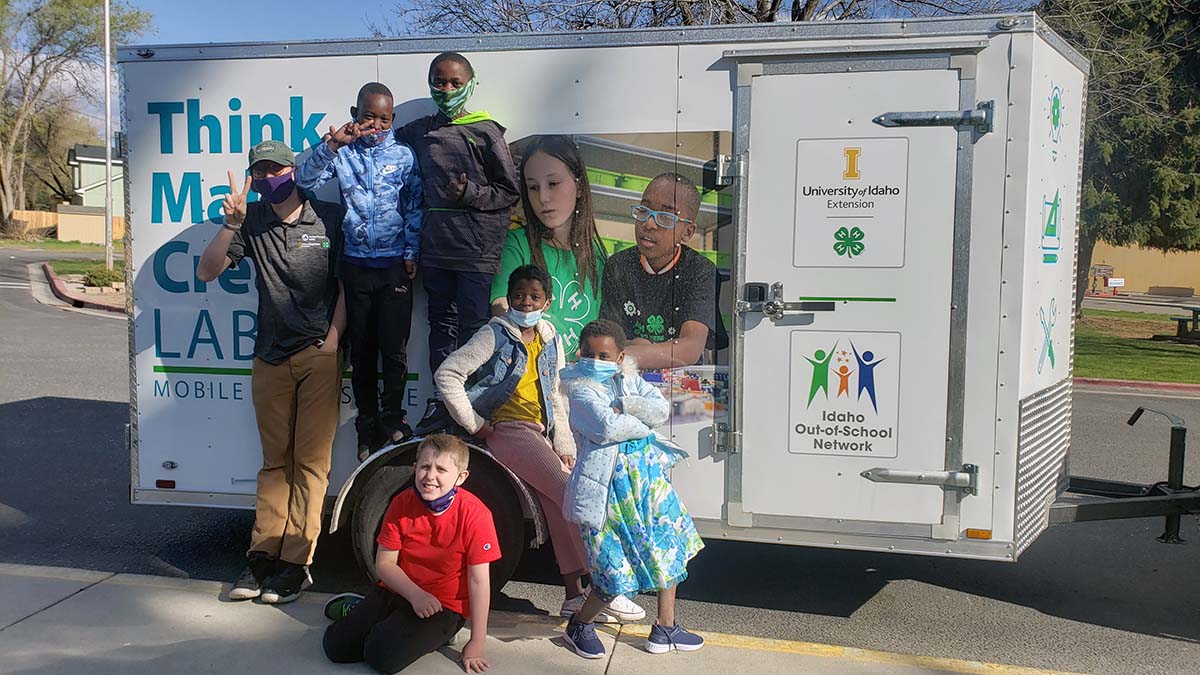 Five children pose around a Think Make Create Lab trailer with an adult wearing a UI Extension shirt.