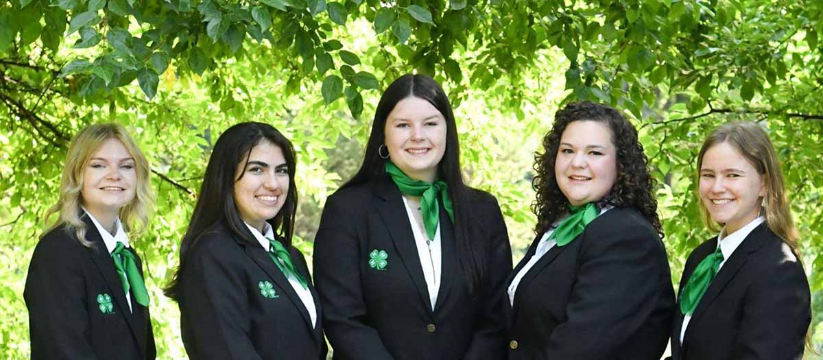 A group of five women wearing black jackets and green scarves.
