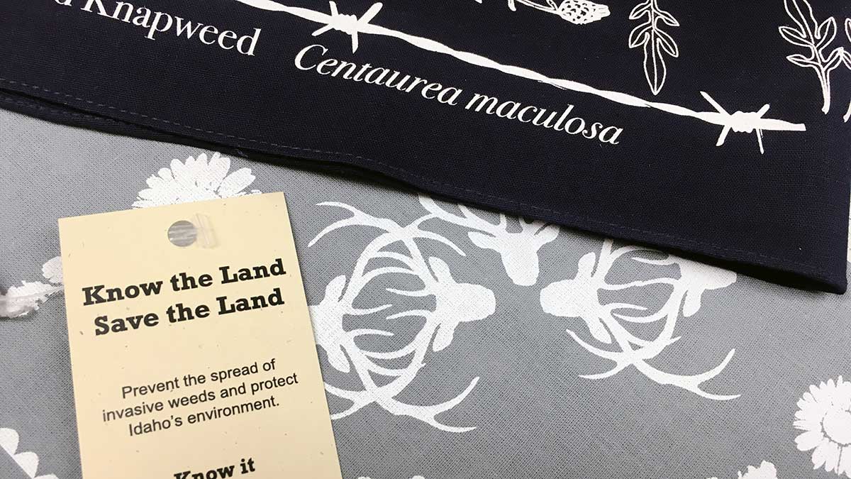 A label that says 'Know the Land, Save the Land, Prevent the spread of invasive weeds and protect Idaho's environment.' Woven cloths with plants and plant names stamped on them.