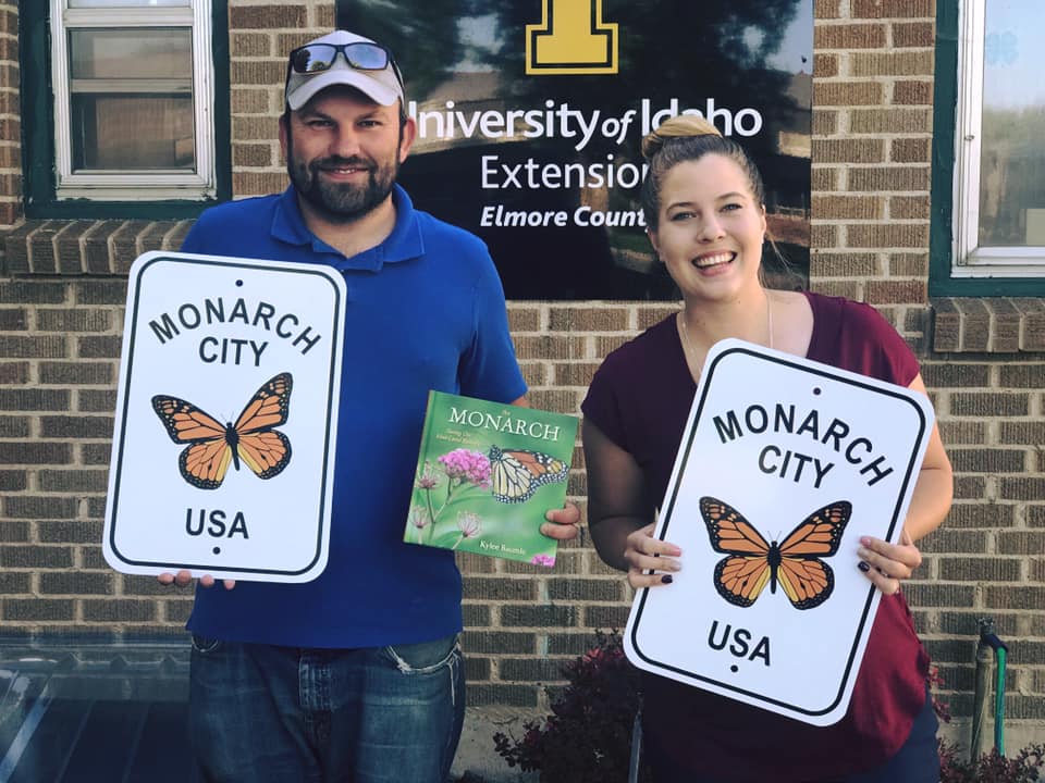 A man and woman hold up road signs that say "Monarch City USA."