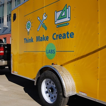 A golden yellow trailer painted with the words Think Make Create.