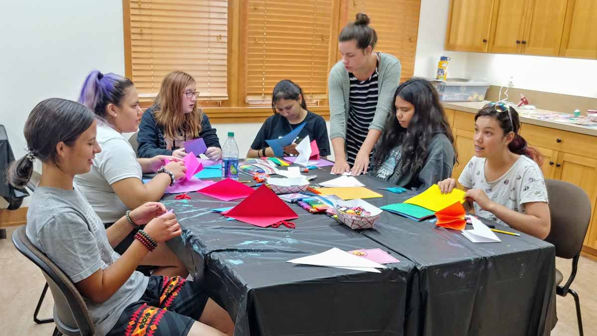 Several young women sit at a table doing paper crafts.