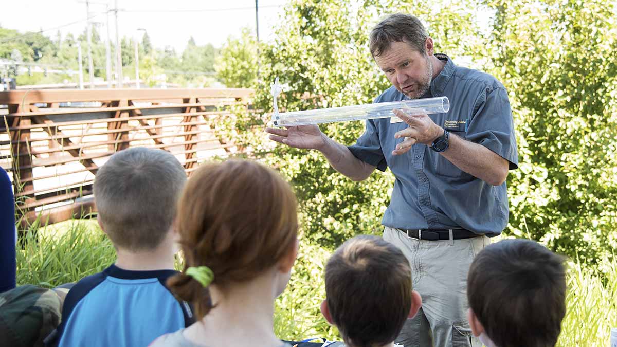 Jim Ekins showing water in a tube with kids