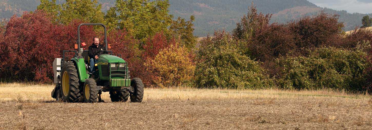 A man drives a farm tractor in an empty field.