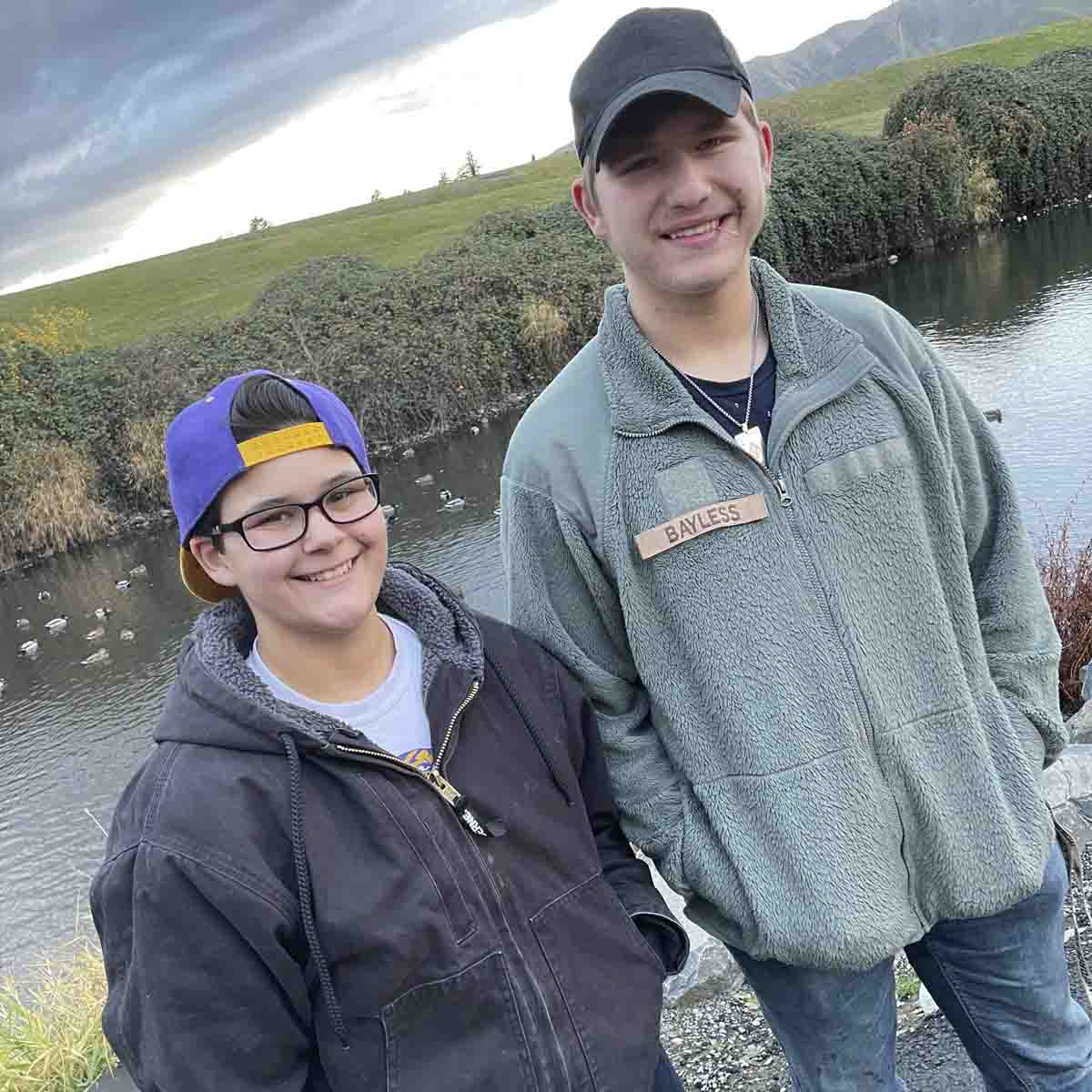 Two high school students stand outside in front of a pond.