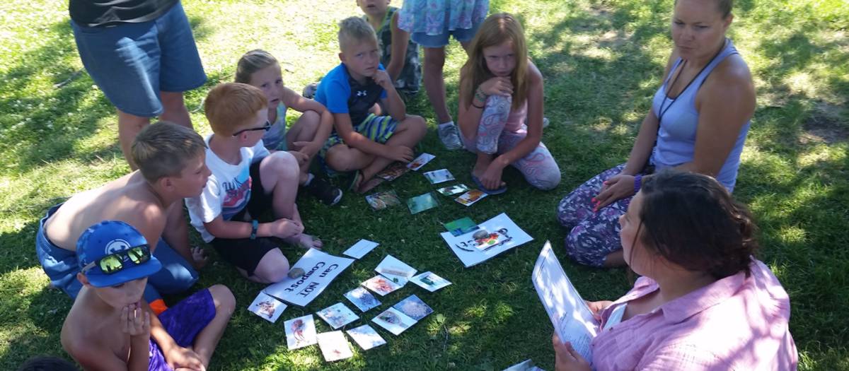 Half a dozen kids and a few adults sit in a circle around cards about composting.