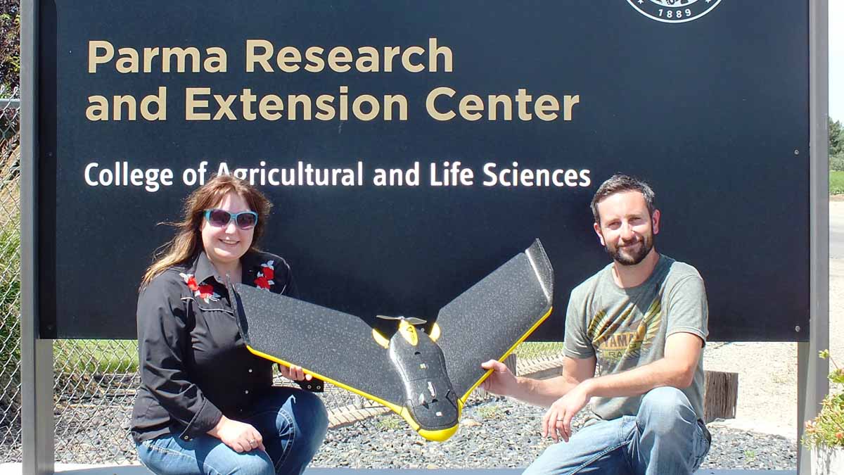 Two people holding a drone in front of the Parma Research and Extension Center sign