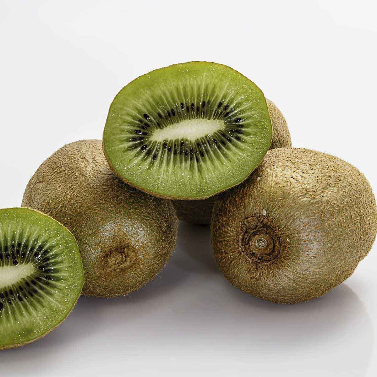 Ripe kiwis on table, some sliced in half to show ripe green and black inside.