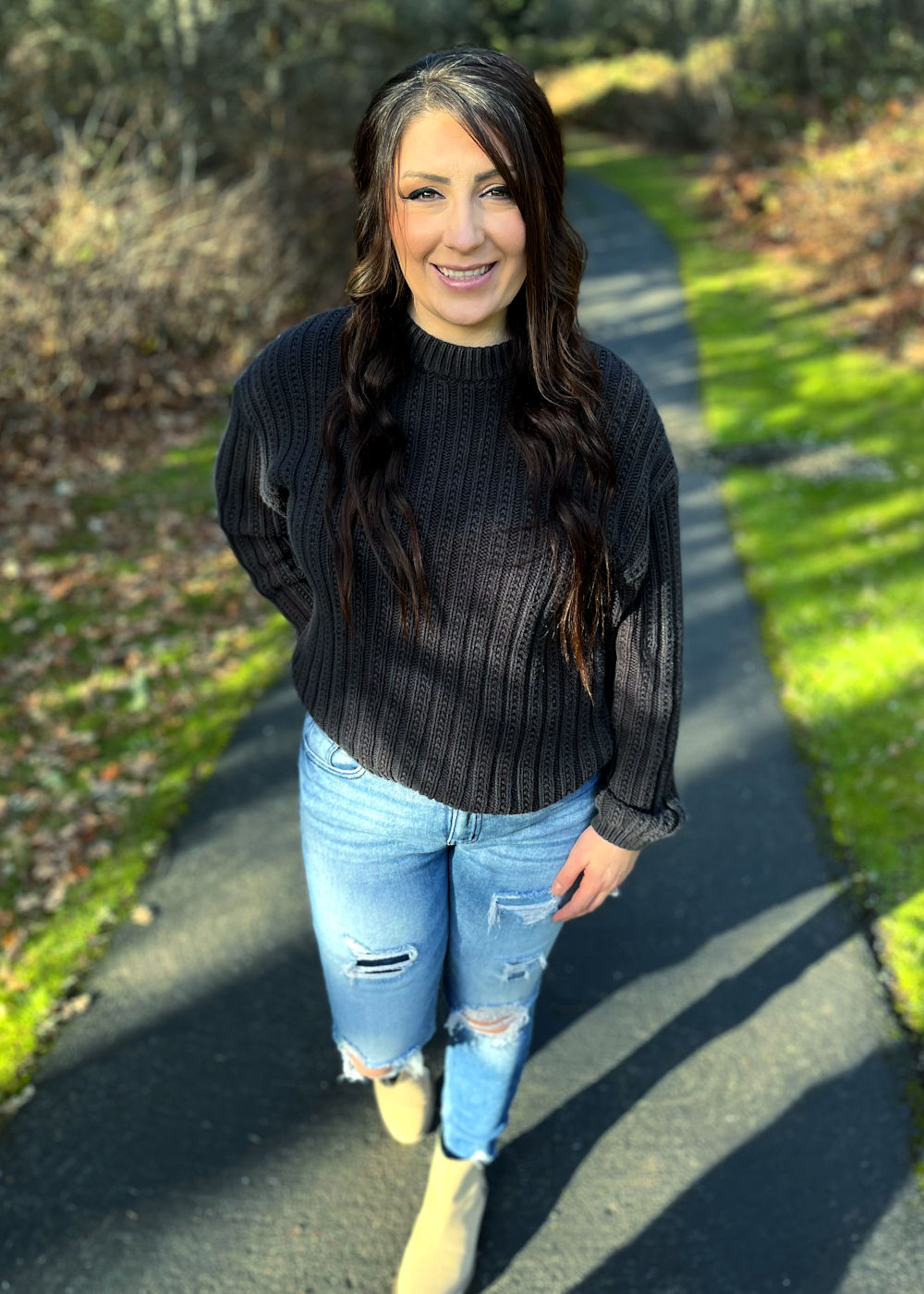 Woman wearing jeans and a sweater stands on a park path.