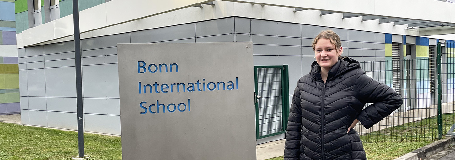 Woman standing in front of Bonn International School sign.