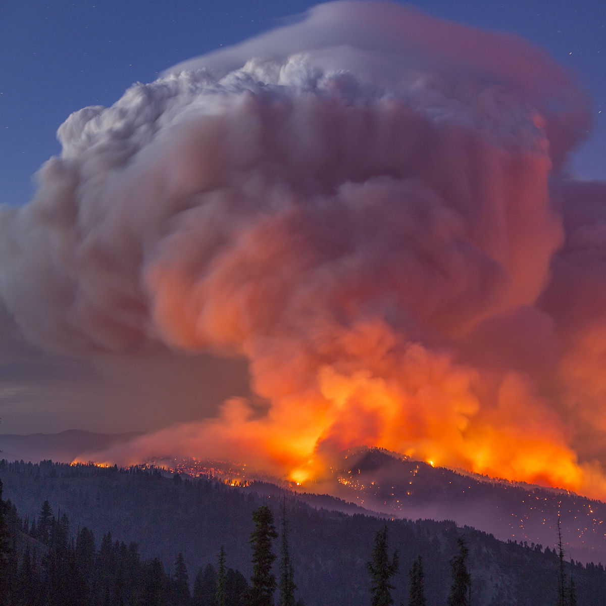 A column of smoke rises from a mountain on fire.