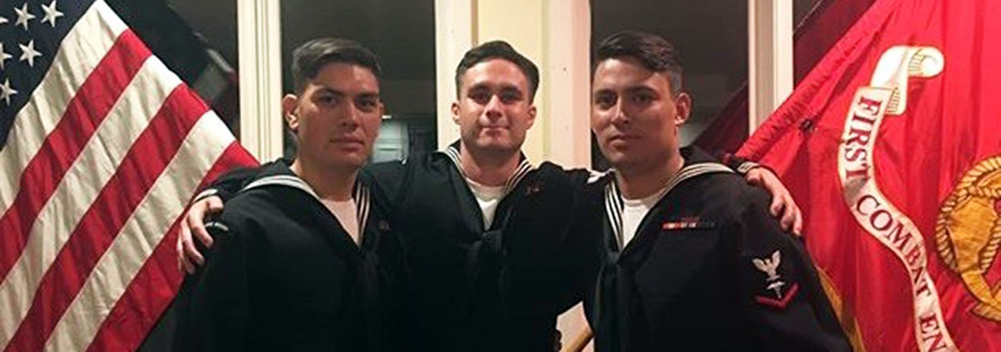 Three men standing between US flag and Navy flag.