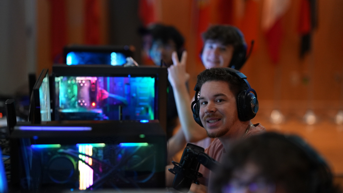 PC gamers smile and give a peace sign to the photographer while sitting at their RGB desktop computers.