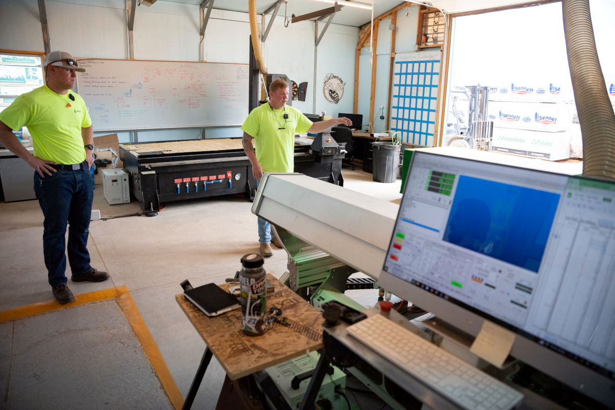 Flashpoint owners Nick Stoppello and Pat Churchman standing in their workshop, a large CNC machine and computer in the forefront.