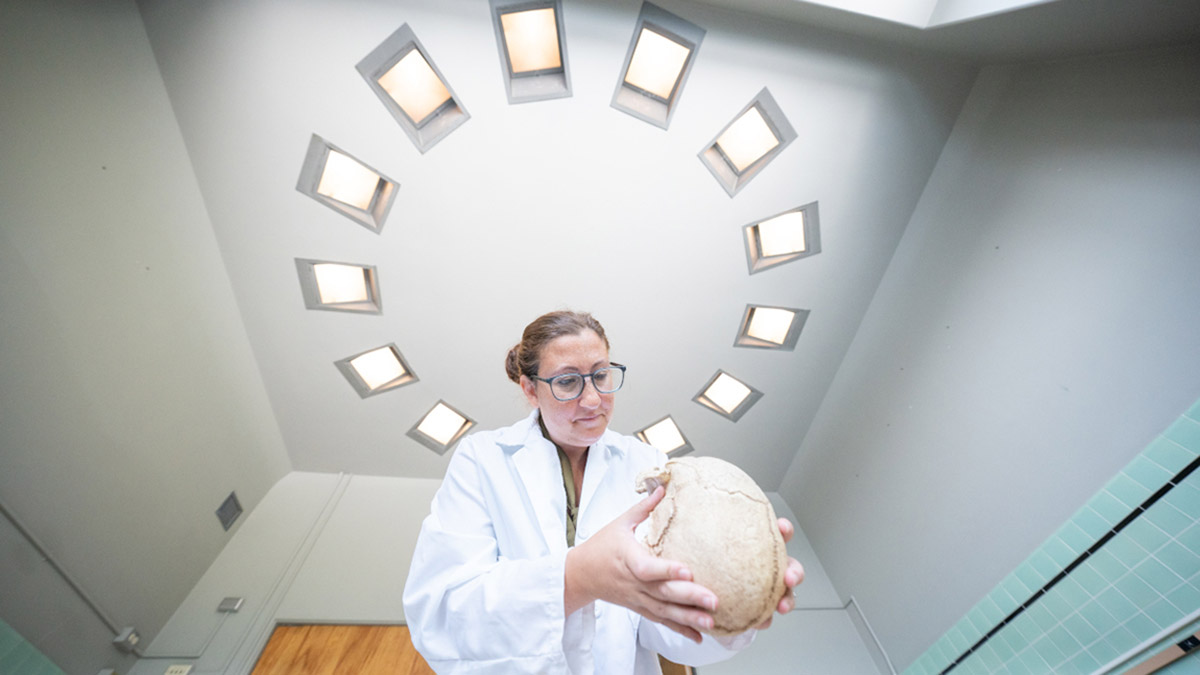 Woman in lab coat examines a human skull