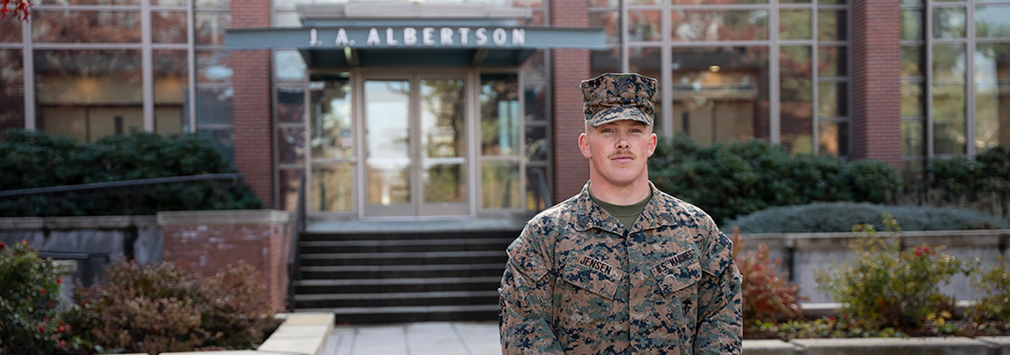 Man wearing battle dress uniform stands in front of Albertson’s Building