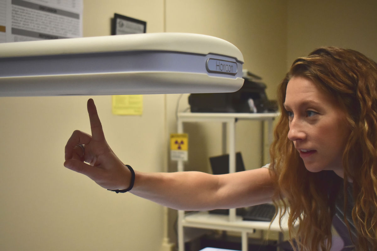 Ann Brown points at a portion of the dual-energy X-ray absorptiometry machine in the Human Performance Lab.