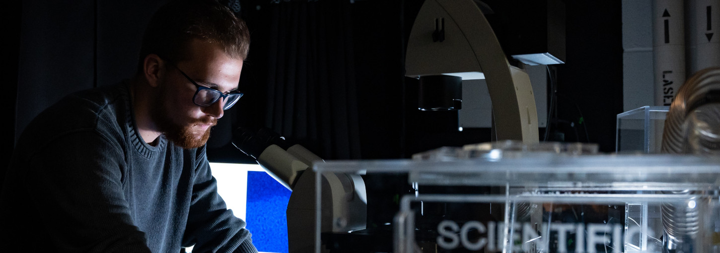 Bearded student wearing spectacles looks into a microscope
