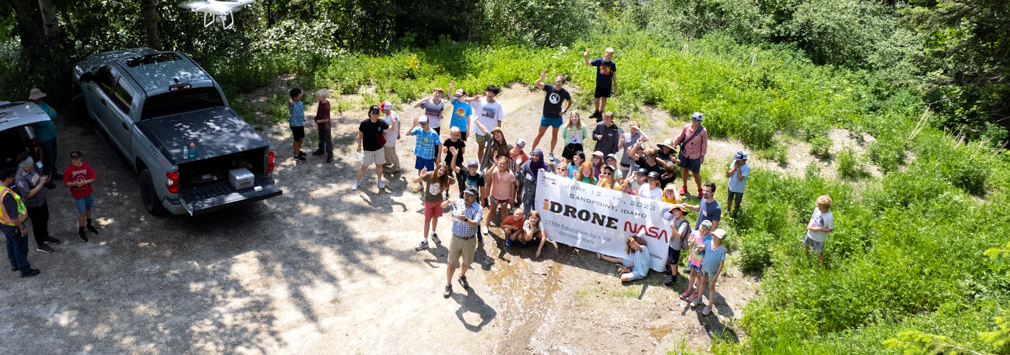 Drone photo of group standing on the ground holding a banner.