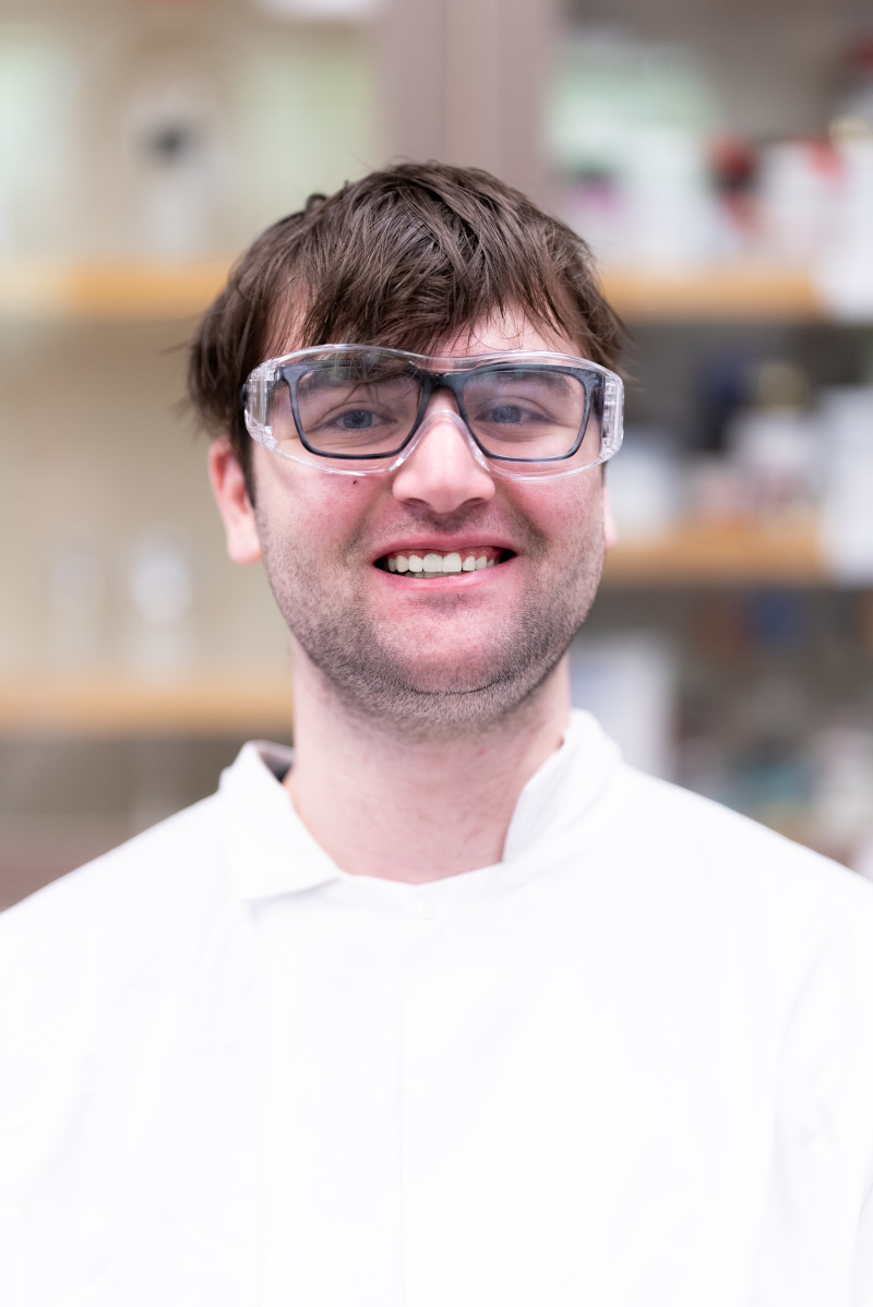 Smiling man in lab coat and safety glasses.