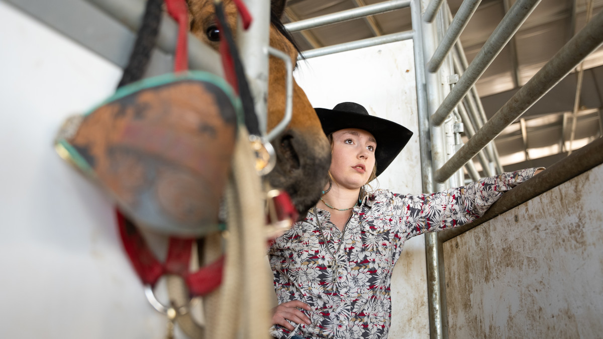 Woman stands in horse stall near horse riding tack.