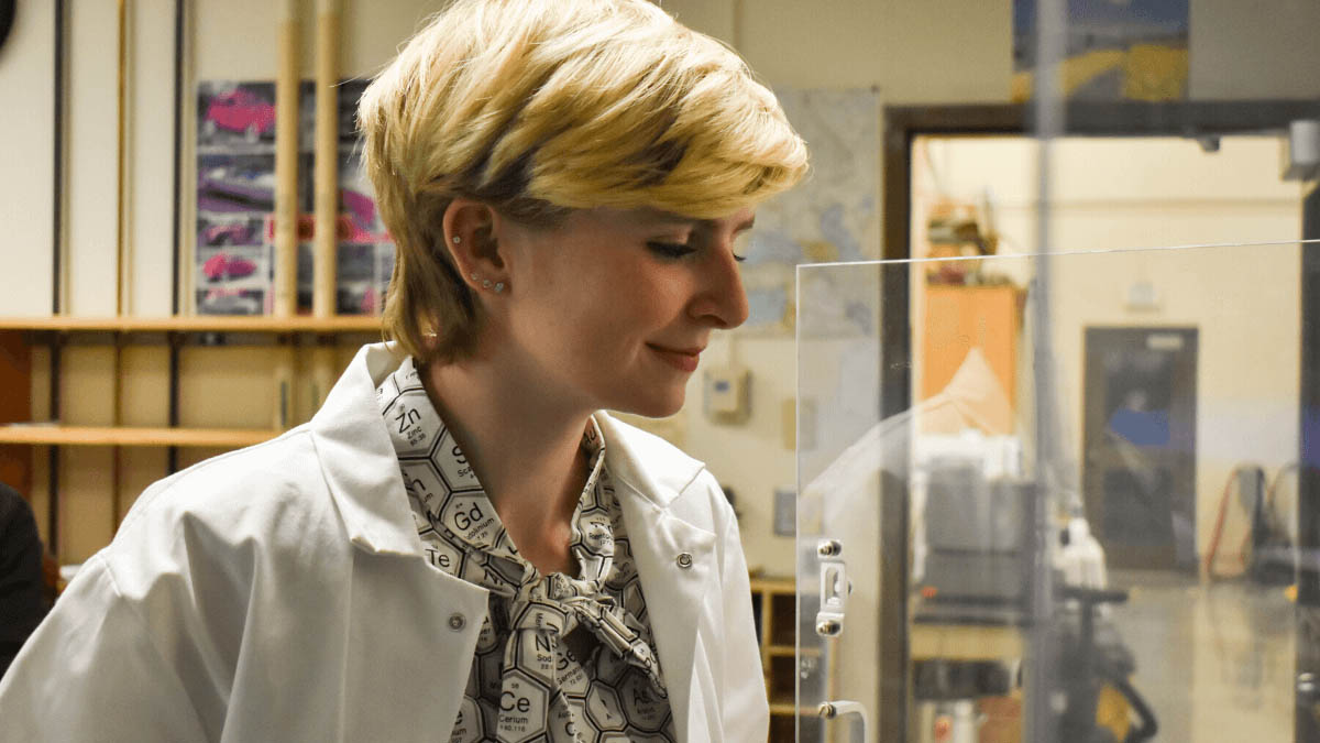 Murphy stands in a lab with her lab coat and a shirt with the periodic table on it.