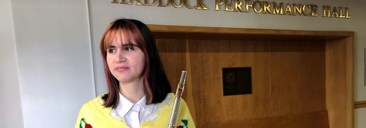 Woman holds flute while standing in the hallway of a music school